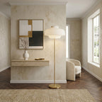 This Clérachic floor lamp lit in a hallway with limewash walls, a herringbone wood floor and a framed abstract print behind it.