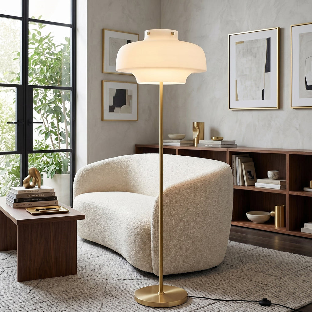 A Clérachic floor lamp with a white glass dome in a bright living room, beside a curved boucle sofa and a walnut shelving unit.