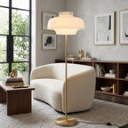 A Clérachic floor lamp with a white glass dome in a bright living room, beside a curved boucle sofa and a walnut shelving unit.