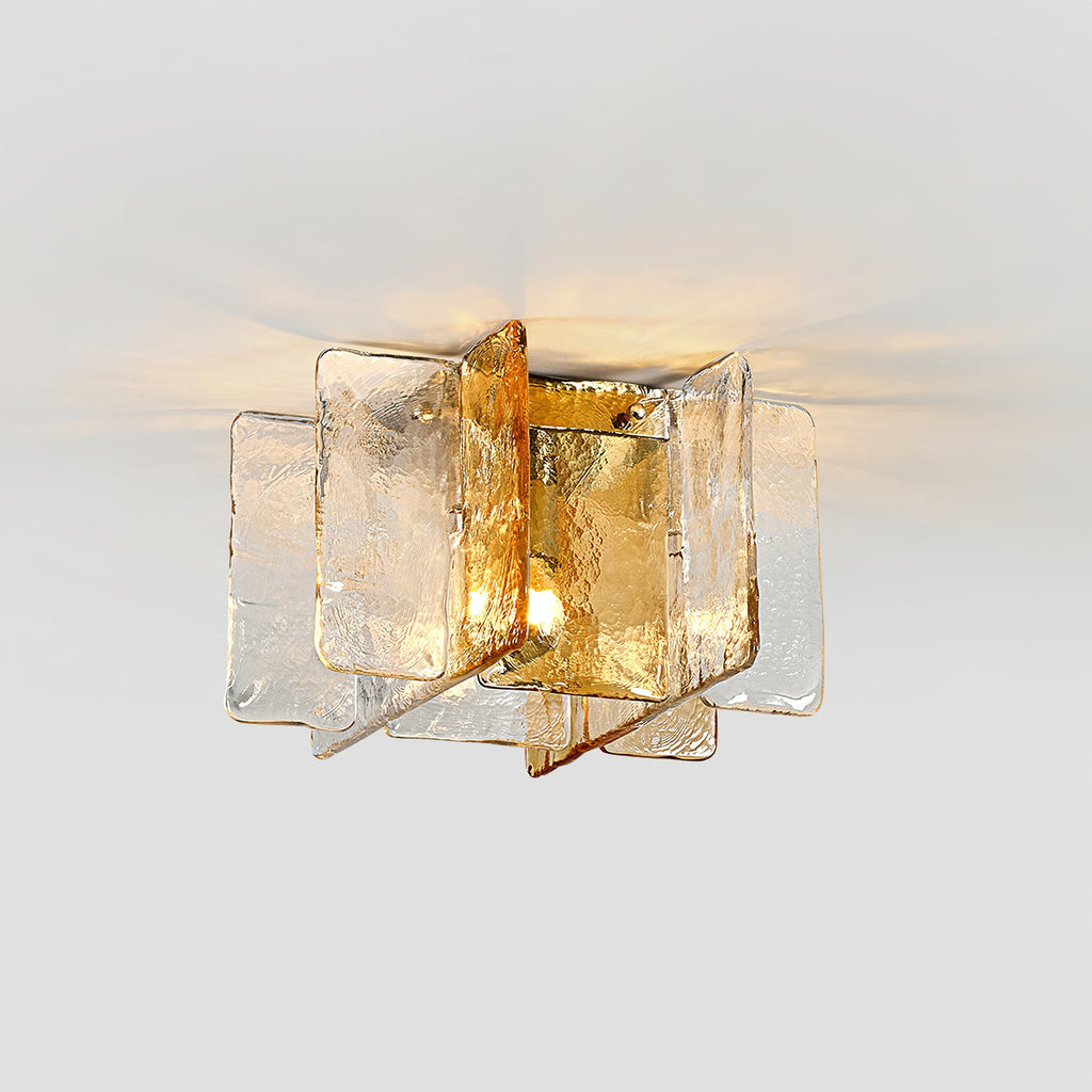 Lit Clérachic ceiling light seen from below, with amber and clear glass panes throwing a warm glow across a pale ceiling.