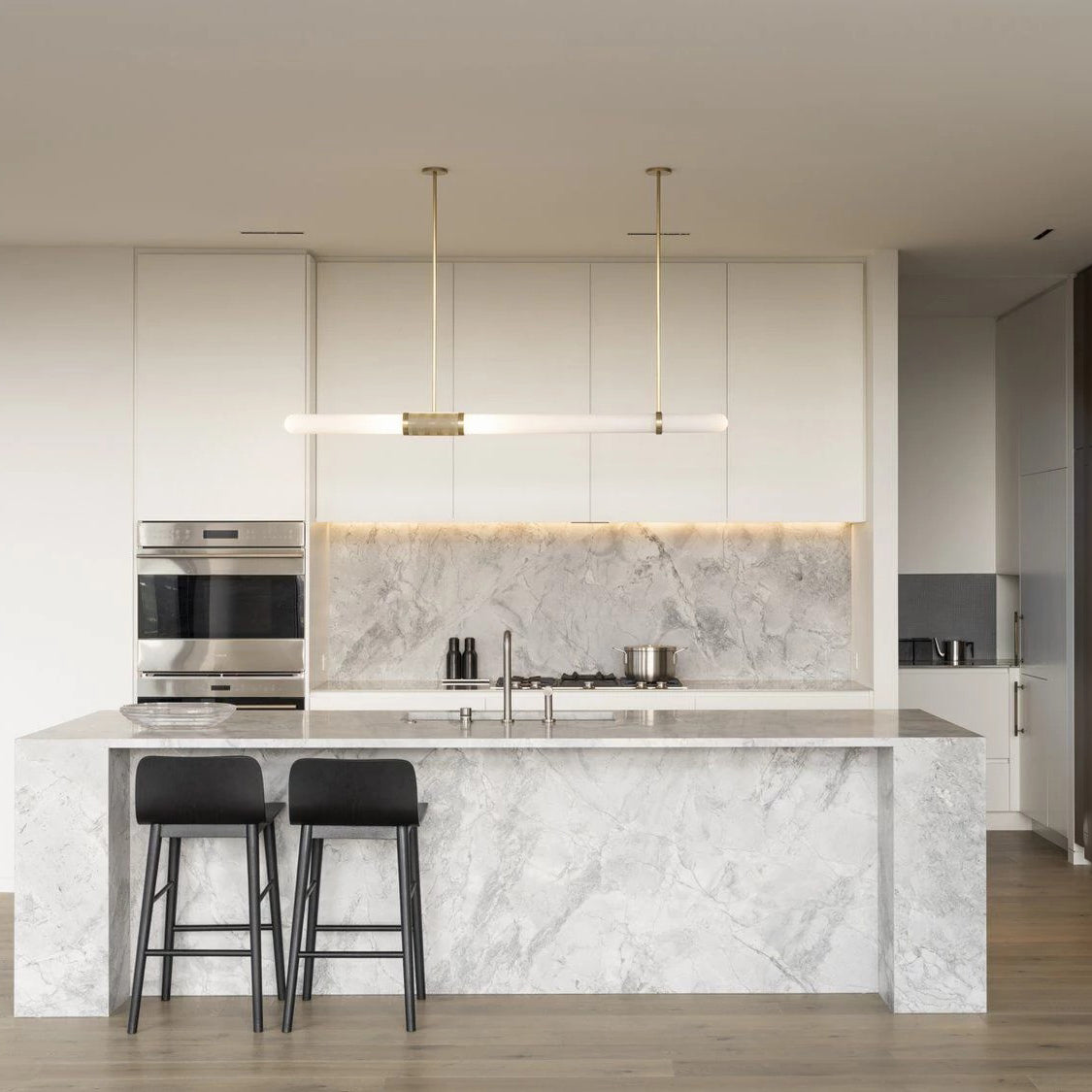 This Clérachic pendant light hangs over a white marble kitchen island, its frosted tube glowing softly beneath two thin gold rods.