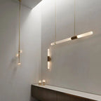 A Clérachic pendant light angled in a pale plaster room beside a lit wall light and a cluster of small glass globes on gold cords.