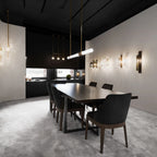 Above a long dark dining table, this Clérachic pendant light hangs in a black-ceilinged showroom with warm wall lights behind it.