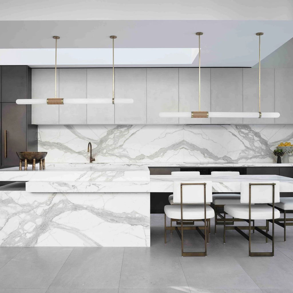 Two Clérachic pendant lights side by side over a long marble island with white and gold dining chairs beneath them.