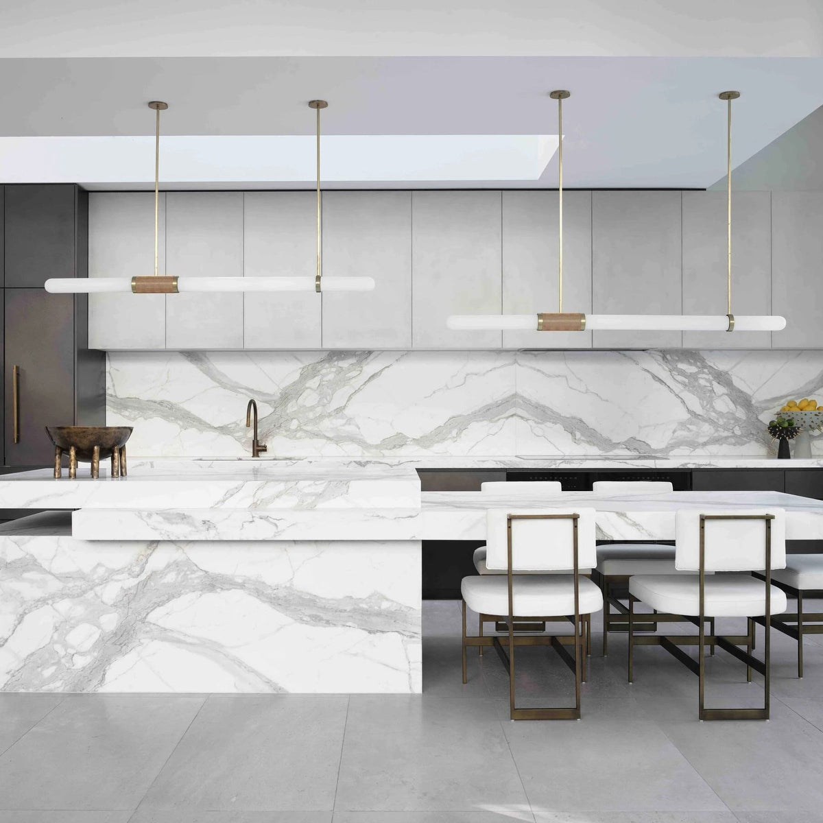 Two Clérachic pendant lights side by side over a long marble island with white and gold dining chairs beneath them.