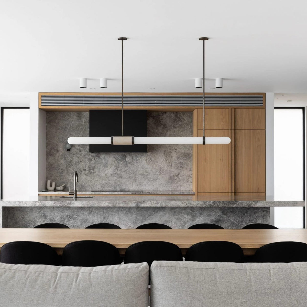 A Clérachic pendant light hangs from dark rods over an oak and stone kitchen island, with a grey sofa in the foreground.