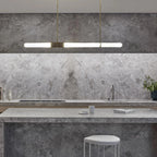 Warm light glows from this Clérachic pendant light, hung above a grey-veined stone splashback and island.