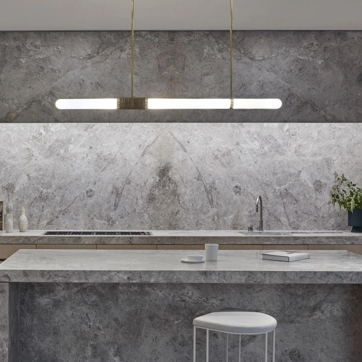 Warm light glows from this Clérachic pendant light, hung above a grey-veined stone splashback and island.