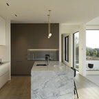 A narrow vertical Clérachic pendant light hangs in a modern kitchen, with a stone-topped island and a dark cabinet wall behind.