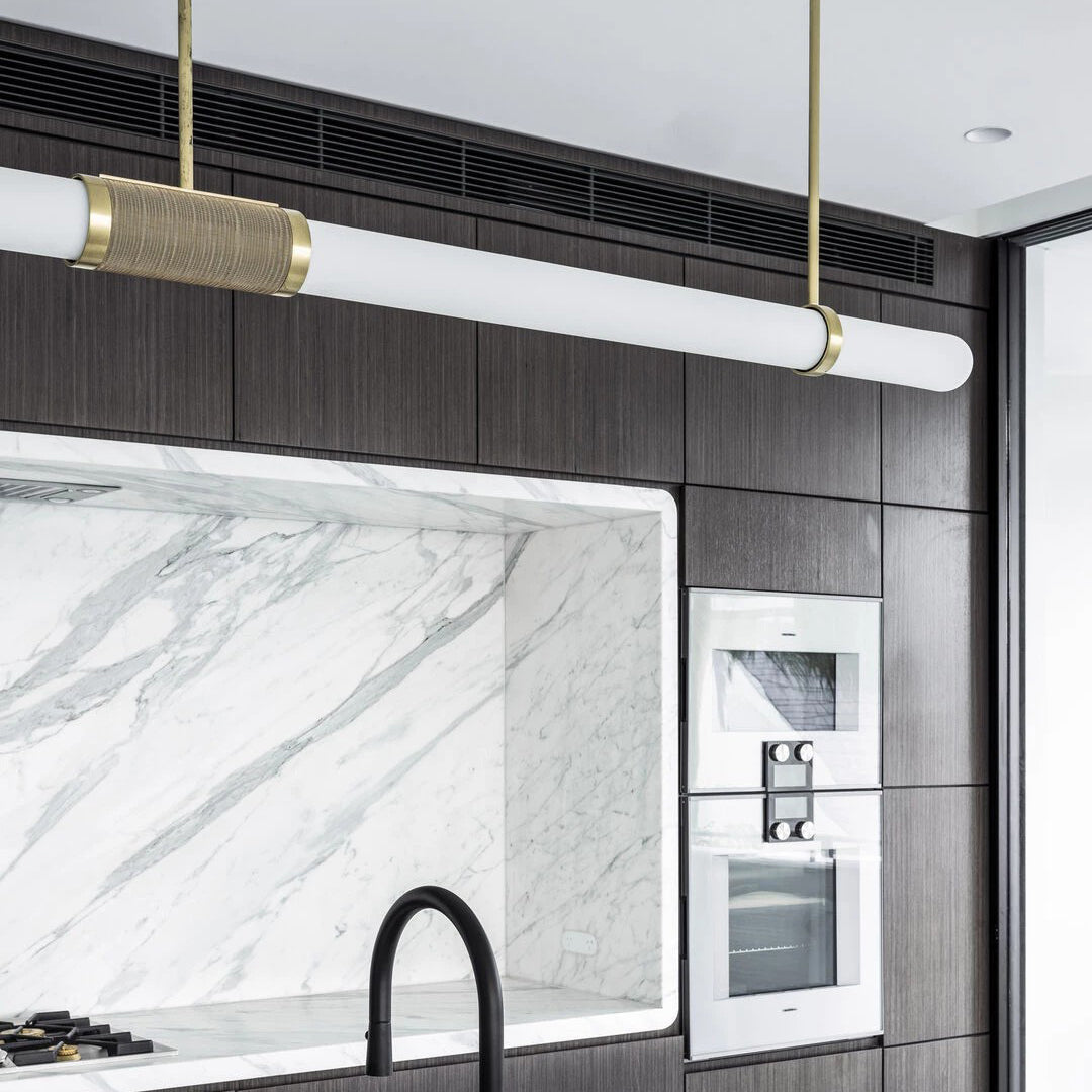 Close view of the gold-and-woven centre band and frosted tube of this Clérachic pendant light in a marble and dark-wood kitchen.