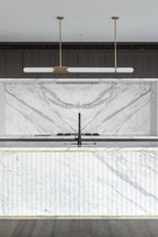 Seen head-on, this Clérachic pendant light spans a marble splashback above a fluted white island with a black tap.