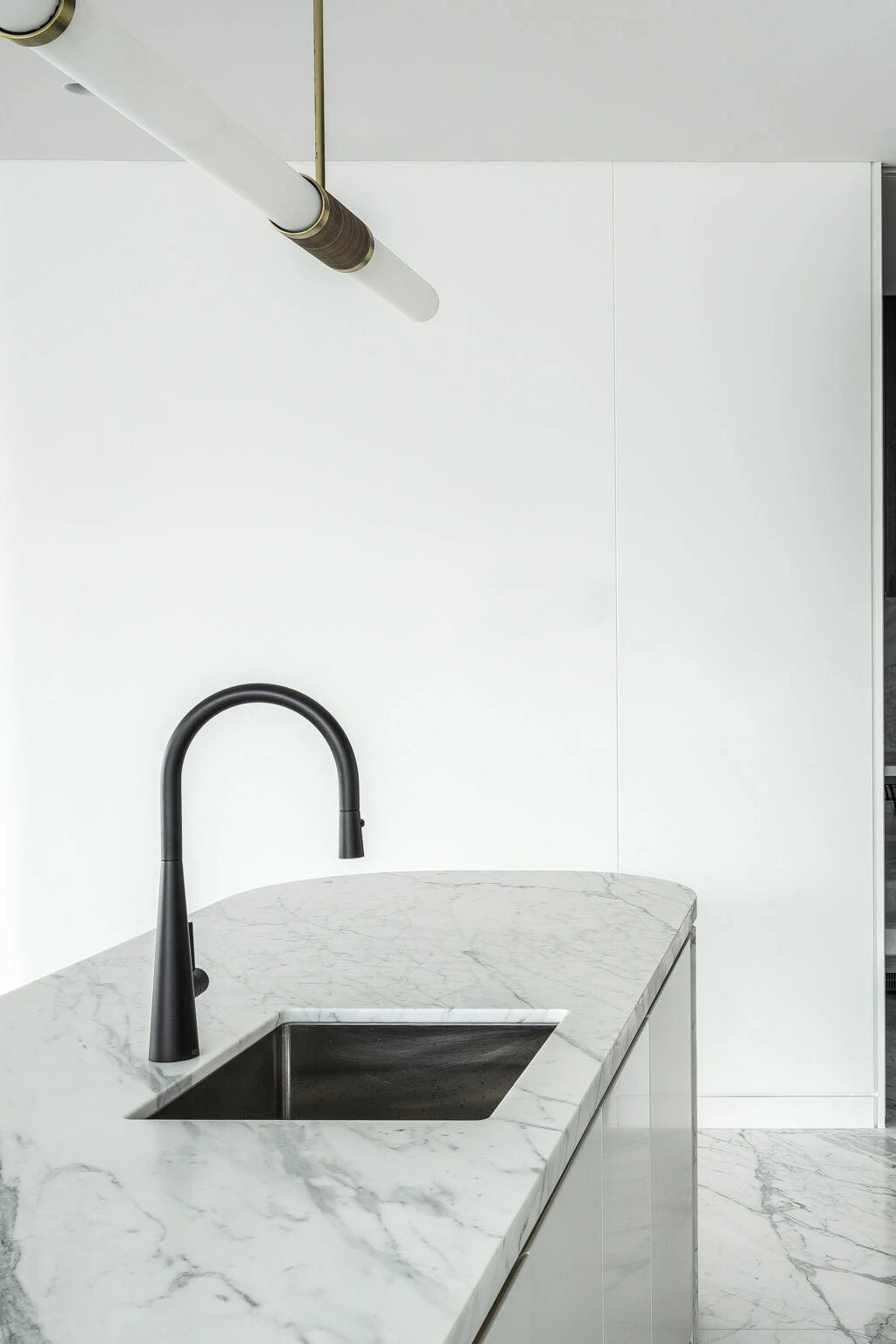 The end of this Clérachic pendant light enters the top of the frame above a marble island with a black pull-down tap.