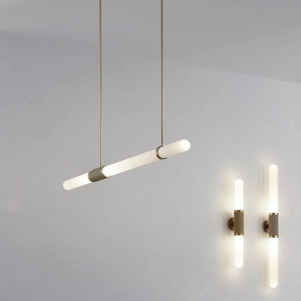 This Clérachic pendant light hangs at a slant on gold rods, two lit wall lights glowing at the lower right.