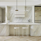 Wide view of a pale stone kitchen with this Clérachic pendant light hung over the cream hood and a curved island below.