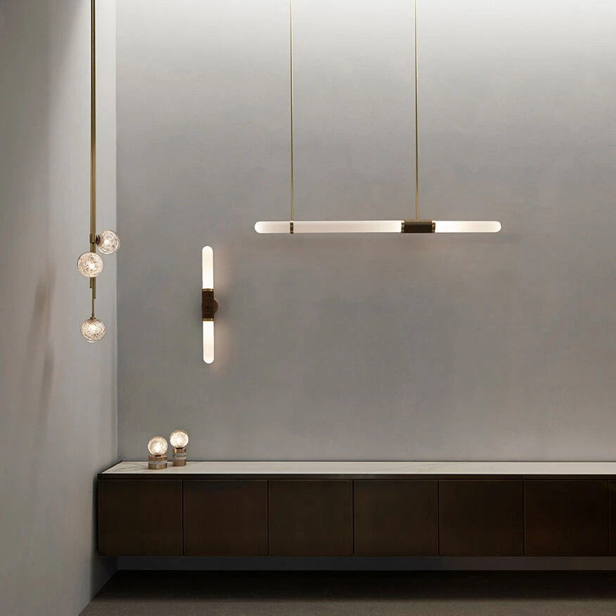 A Clérachic pendant light lit against a grey wall, beside a wall light and small glass globes above a floating dark cabinet.