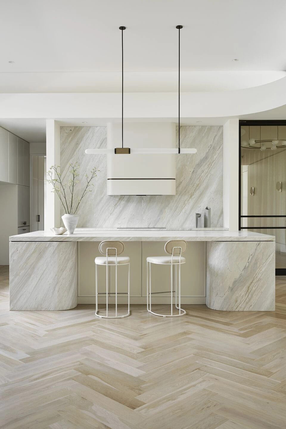 Tall view of a cream stone kitchen, with this Clérachic pendant light small and central above a curved island and herringbone floor.