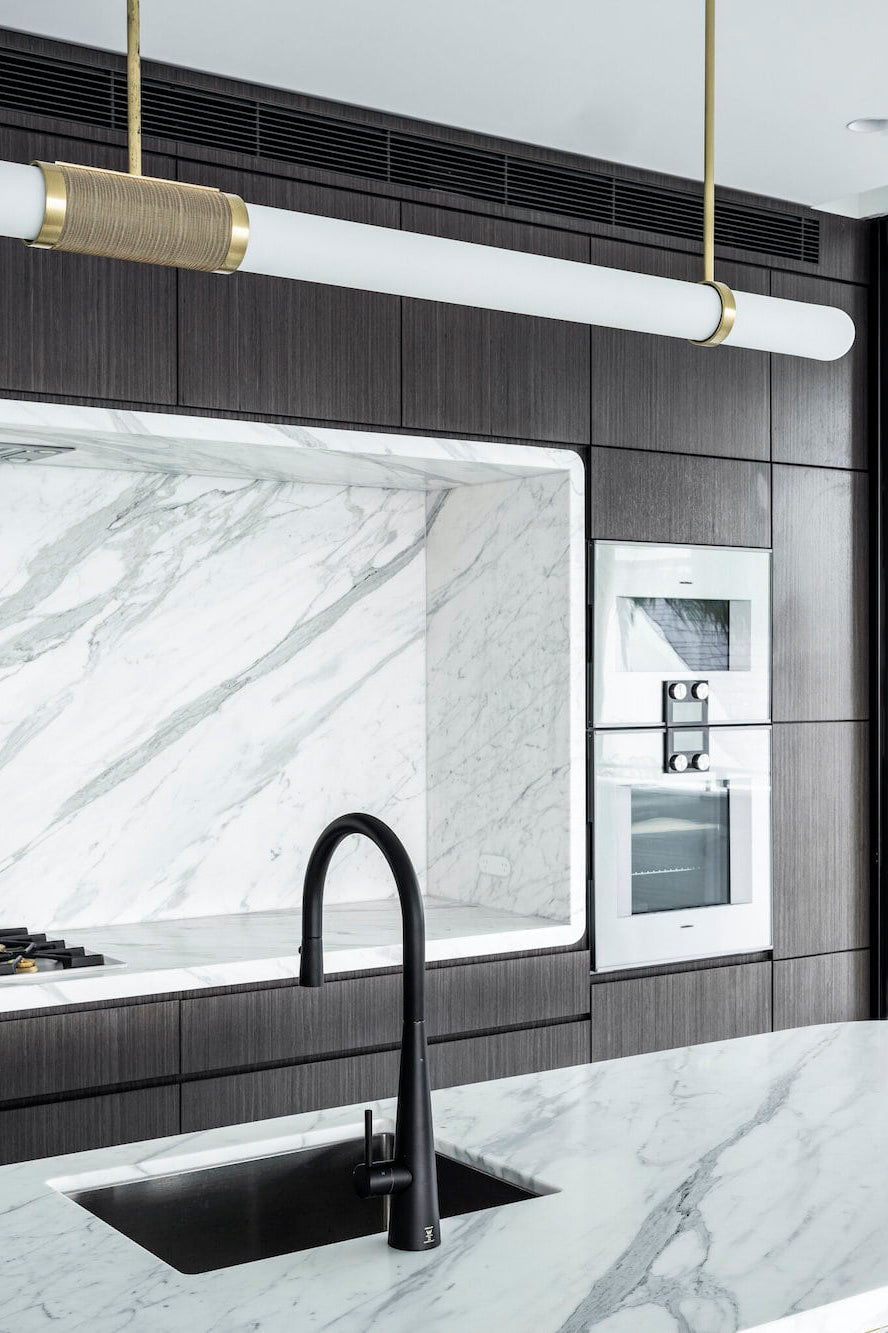 Close view of this Clérachic pendant light overhead, its woven band catching light above a black tap and marble worktop.