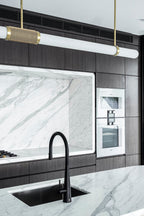 Close view of this Clérachic pendant light overhead, its woven band catching light above a black tap and marble worktop.