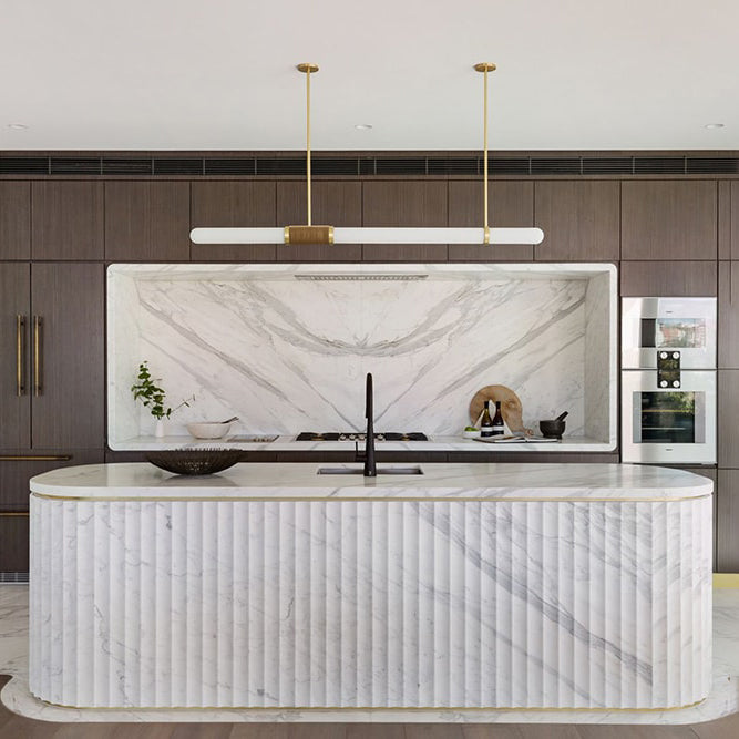This Clérachic pendant light hangs over a fluted white marble island, with a recessed marble splashback and oak cabinetry behind.