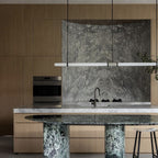 A Clérachic pendant light spans a timber kitchen above a green marble-topped island with dark-green stone legs.