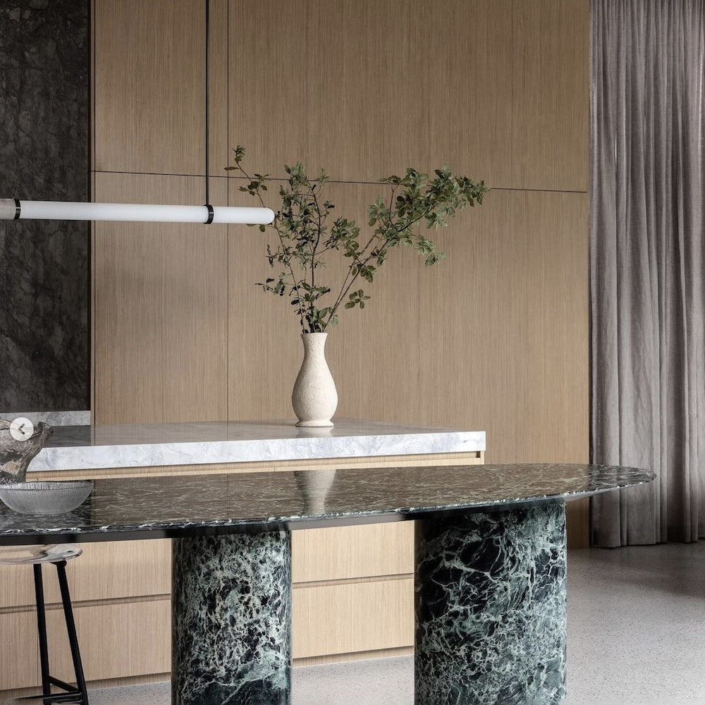 This Clérachic pendant light enters from the left above a green marble table, with a slim vase of branches in front of oak panelling.
