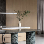 This Clérachic pendant light enters from the left above a green marble table, with a slim vase of branches in front of oak panelling.