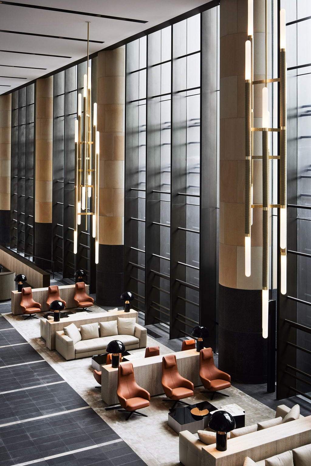 Tall stacked tubes of this Clérachic pendant light fall through a double-height lobby with leather armchairs and large windows.