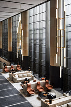 Tall stacked tubes of this Clérachic pendant light fall through a double-height lobby with leather armchairs and large windows.