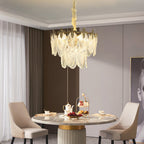 This Clérachic glass leaf chandelier hangs above a round marble dining table set with a tea stand and beige upholstered chairs.