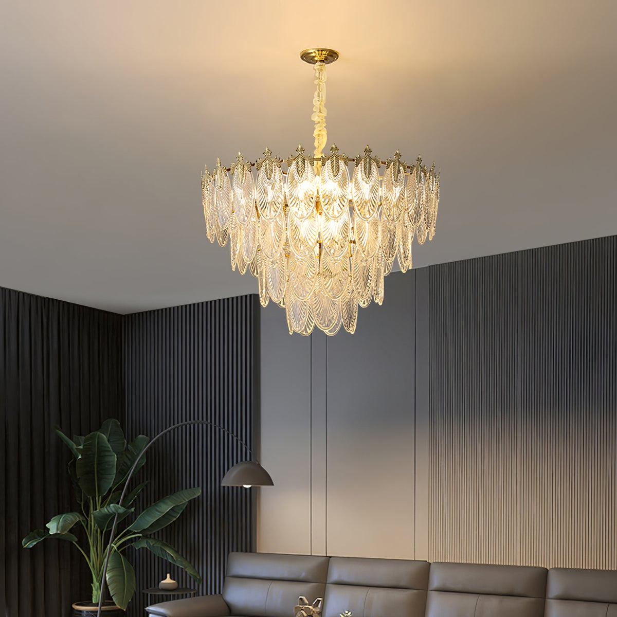 A Clérachic chandelier with layered glass leaves glows in a dark-panelled lounge, with a leather sofa and a tall plant below.
