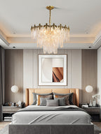 Clérachic leaf chandelier lit above a bed with a tan headboard and grey bedding, in a bedroom with a recessed ceiling and framed art.