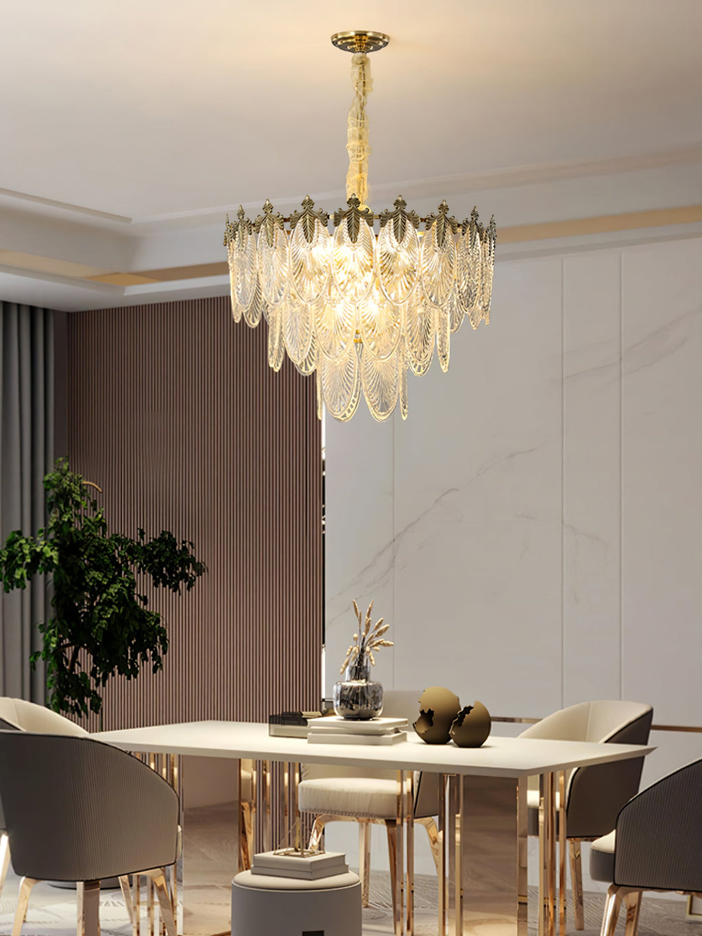 This Clérachic chandelier hangs over a pale dining table with gilded chair legs, with a potted plant at the left and marble wall behind.