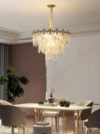 This Clérachic chandelier hangs over a pale dining table with gilded chair legs, with a potted plant at the left and marble wall behind.