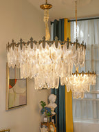 Two sizes of Clérachic glass leaf chandelier hang together in one room, with a teal and yellow curtain and a framed picture below.