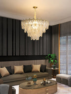 A Clérachic chandelier lights a lounge with striped dark wall panels, an olive sofa with tan cushions and an oval gold coffee table.
