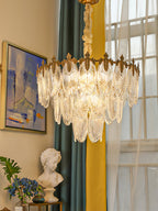 Close, lit view of this Clérachic chandelier in a room with a teal and yellow curtain, a seascape painting and a white bust on a stand.
