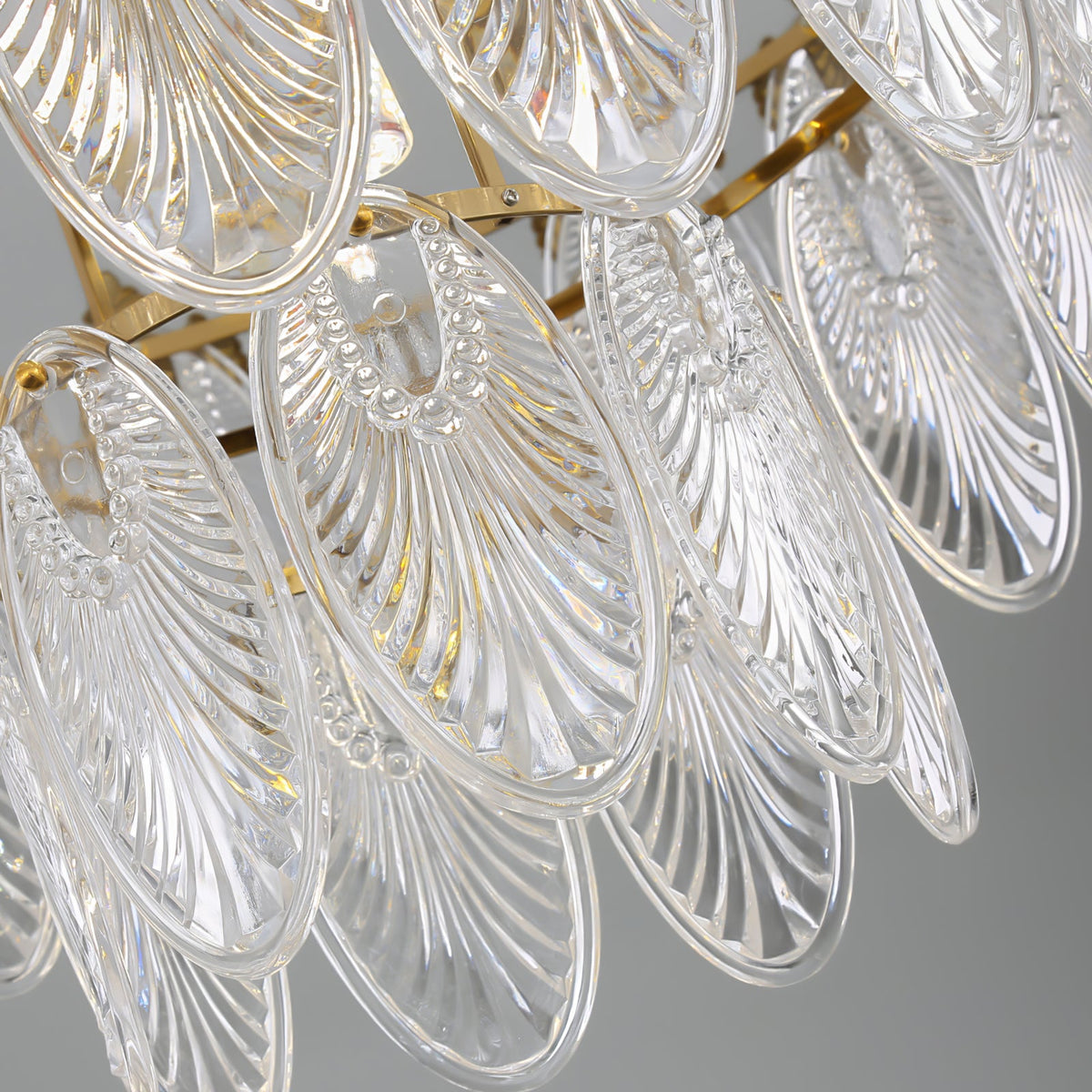 Close view of the ribbed, shell-shaped glass leaves on this Clérachic chandelier, held on a gold frame, shown against a grey backdrop.