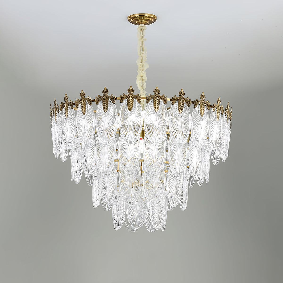 Unlit Clérachic chandelier on a grey backdrop, its glass leaves stepped in several tiers below the gold canopy and chain.