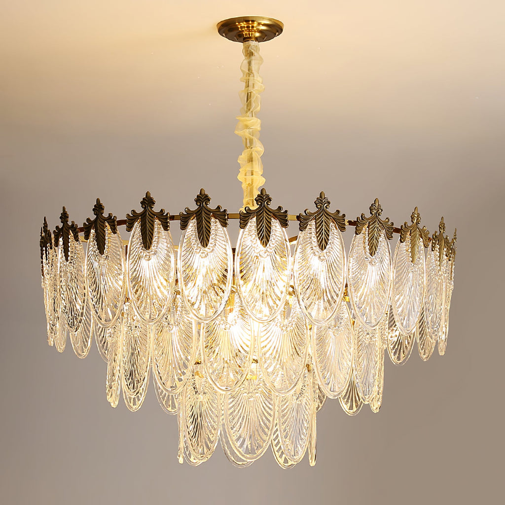 Lit Clérachic chandelier glowing warm against a cream ceiling, showing its broad tiers of glass leaves under a gold crown.