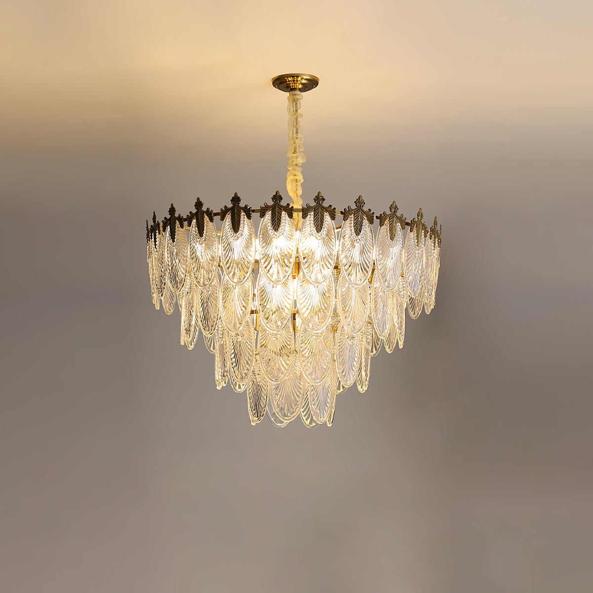 Warm light shining through the layered glass leaves of this Clérachic chandelier, with the gold crown at the top and a pale ceiling above.