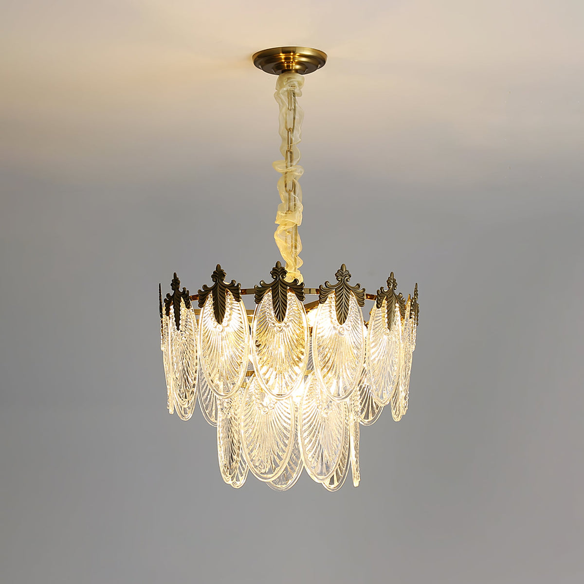 Two-tier Clérachic chandelier lit on a grey backdrop, with a long pale chain and glass leaves glowing at the lower edge.