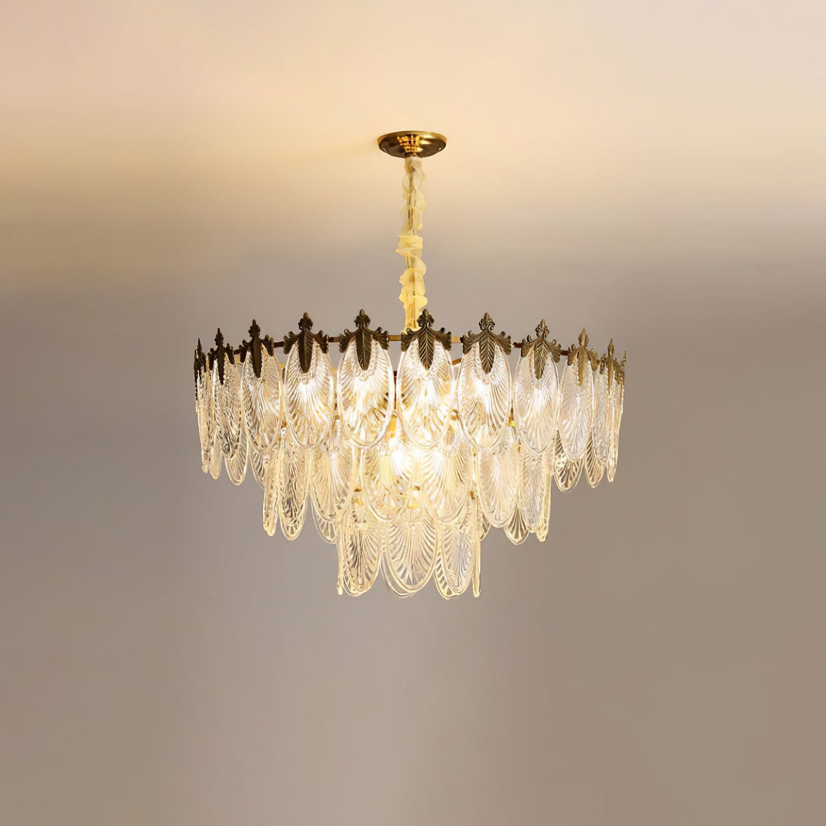 Lit Clérachic chandelier seen straight on, with its glass leaves layered in three tiers and a warm glow on the ceiling behind.