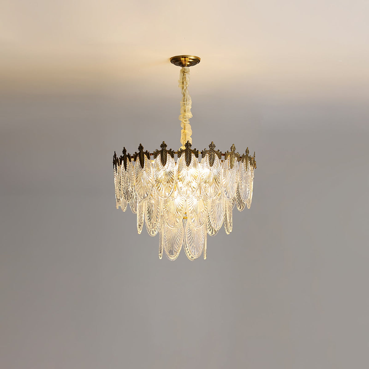 Lit mid-size Clérachic chandelier on a grey backdrop, its three tiers of clear leaf shades hanging below a gold canopy.