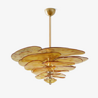 A Clérachic chandelier on a white backdrop, with amber-gold glass petals stacked in tiers around a brass rod and a brass ceiling cup.