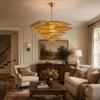 Amber glass petal chandelier from Clérachic lit above a coffee table in a traditional living room with a cream sofa and a landscape painting.