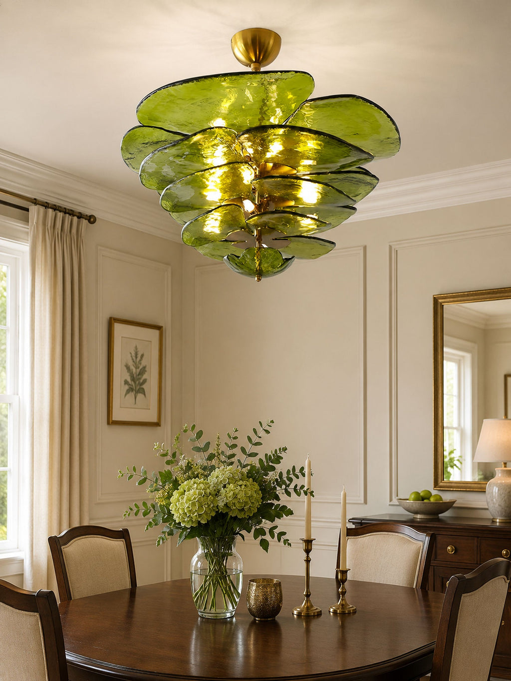 Green and gold Clérachic chandelier hanging over a dark round dining table with a vase of hydrangeas and brass candlesticks.