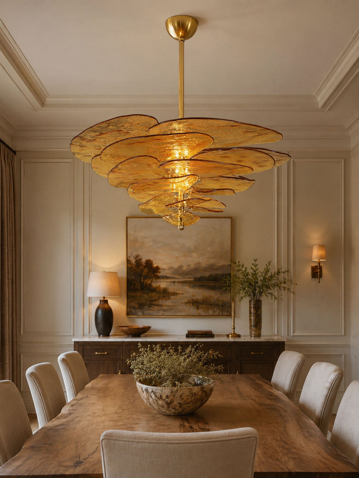 Amber Clérachic chandelier lit over a long wooden dining table in a panelled room, with a landscape painting on the far wall.