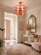 A pink Clérachic petal chandelier lights a hallway with a blush front door, a mirror, a console table and a pink armchair.
