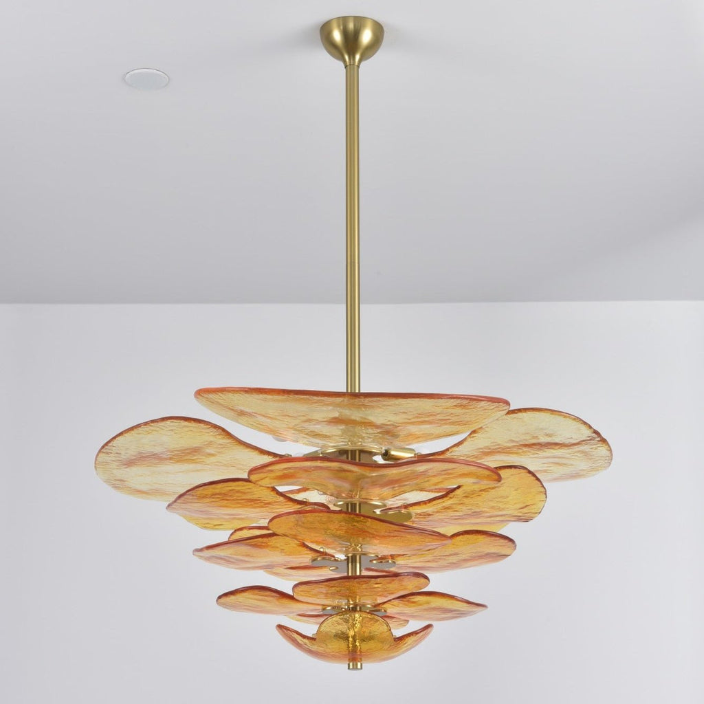 Amber Clérachic chandelier on a plain grey backdrop, its apricot-tinged glass petals stacked below a long brass rod.