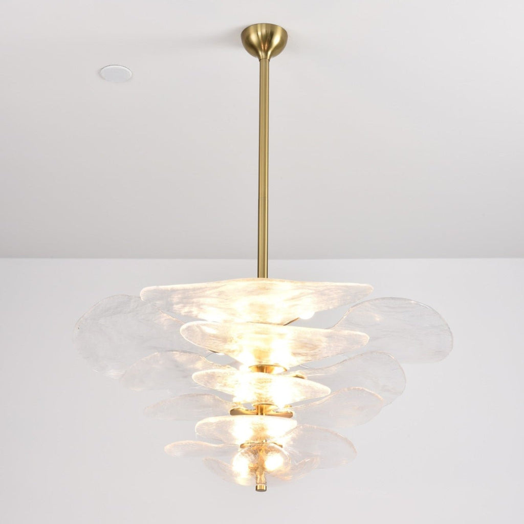 Lit clear glass Clérachic chandelier on a long brass rod, with soft white petals and bulbs glowing between the tiers.